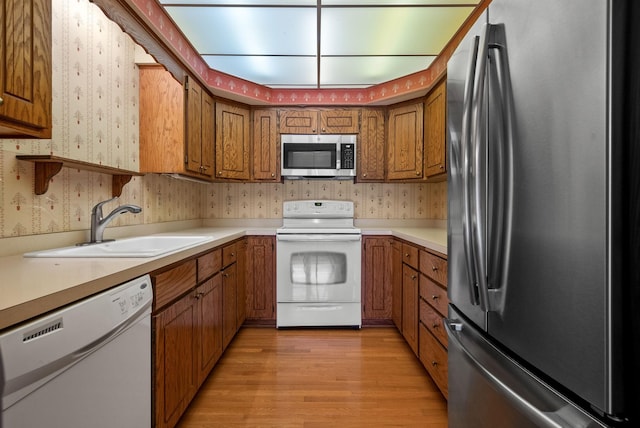 kitchen with stainless steel appliances, a sink, brown cabinetry, and wallpapered walls