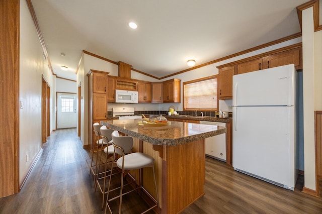kitchen featuring dark wood-style flooring, ornamental molding, white appliances, a kitchen island, and brown cabinetry