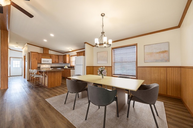 dining space featuring ceiling fan with notable chandelier, crown molding, a wainscoted wall, and dark wood finished floors