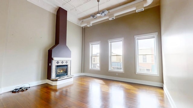 unfurnished living room with a tile fireplace, a wealth of natural light, and wood finished floors