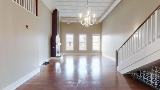 unfurnished living room featuring baseboards, wood finished floors, a towering ceiling, and a notable chandelier