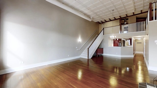 unfurnished living room with baseboards, wood finished floors, a towering ceiling, and stairway