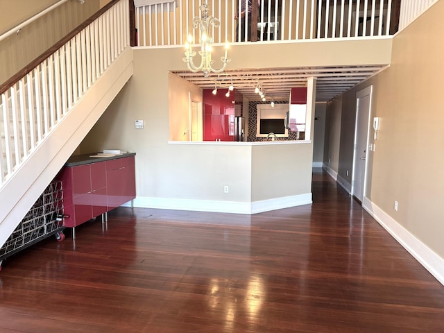 unfurnished living room featuring a chandelier, hardwood / wood-style floors, a towering ceiling, and baseboards