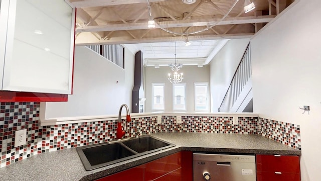 kitchen with dark countertops, stainless steel dishwasher, a sink, and backsplash