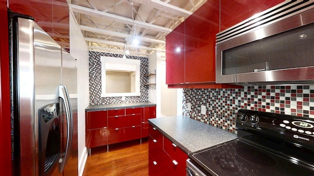 kitchen featuring red cabinetry, dark countertops, wood finished floors, decorative backsplash, and appliances with stainless steel finishes