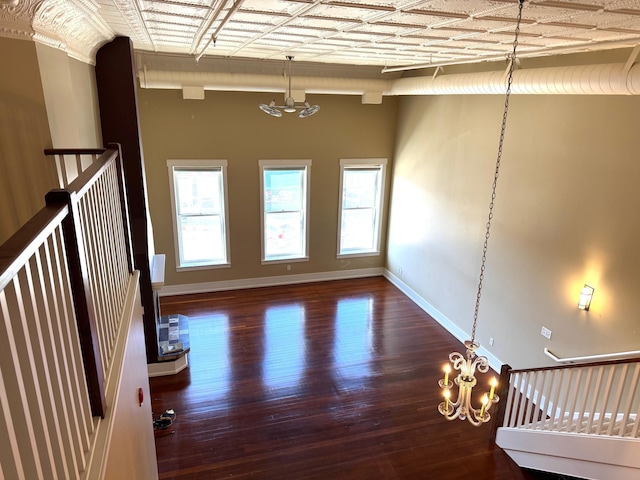 empty room featuring baseboards, wood finished floors, a wealth of natural light, and an inviting chandelier
