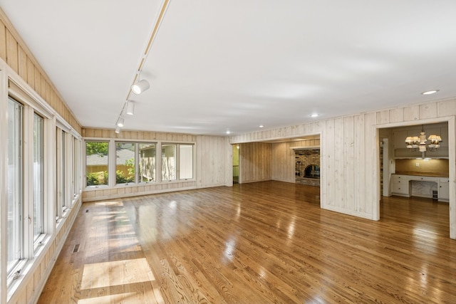 13907 Mcginty Rd E, Minnetonka, MN 55305 - unfurnished living room featuring wood finished floors, track lighting, a fireplace, a chandelier, and wooden walls
