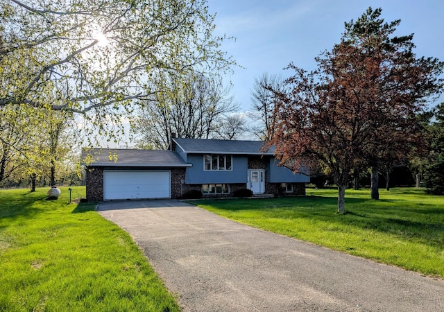 raised ranch featuring an attached garage, driveway, a front yard, and brick siding
