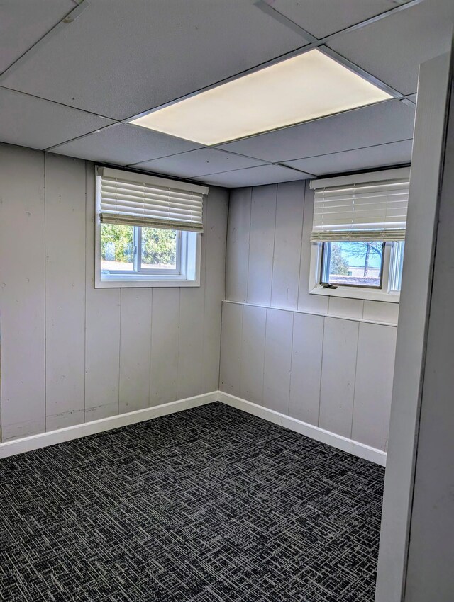 below grade area featuring plenty of natural light, carpet, baseboards, and a paneled ceiling