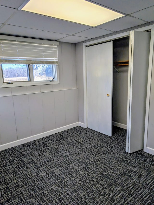 unfurnished bedroom with dark carpet, a drop ceiling, a closet, and baseboards