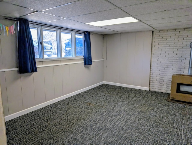 unfurnished room featuring a wood stove, carpet, a drop ceiling, and baseboards