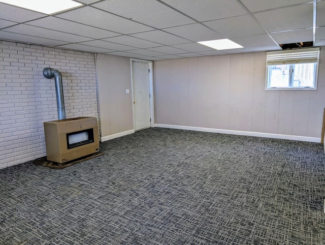 basement featuring a wood stove, carpet flooring, a drop ceiling, and heating unit