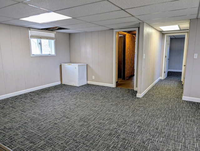 basement featuring carpet flooring, white refrigerator, baseboards, and a drop ceiling