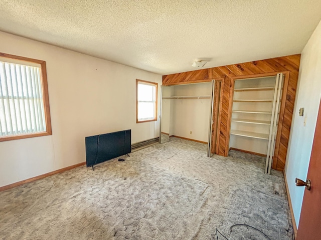 unfurnished bedroom with a textured ceiling, two closets, carpet floors, and baseboards