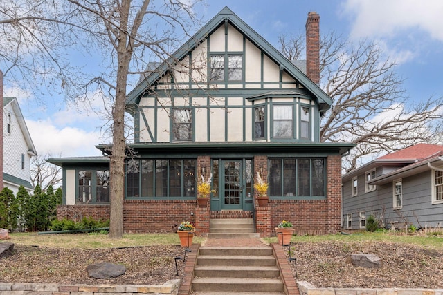 tudor home featuring a sunroom, a chimney, stucco siding, and brick siding