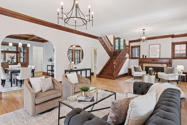 living area with light wood-type flooring, crown molding, a notable chandelier, and arched walkways