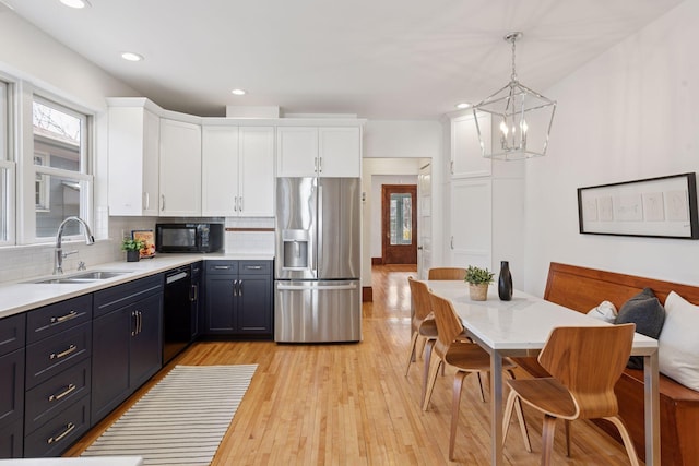 kitchen with an inviting chandelier, a sink, black appliances, backsplash, and white cabinetry