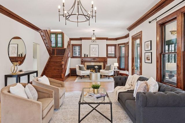 living area featuring a chandelier, light wood-style floors, crown molding, stairs, and a lit fireplace