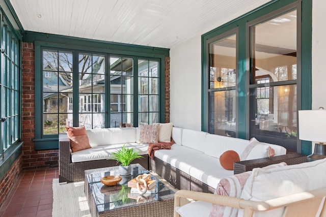 sunroom / solarium featuring tile patterned floors, a wealth of natural light, an outdoor hangout area, and brick wall