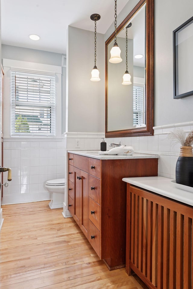 bathroom with wood finished floors, tile walls, a wainscoted wall, toilet, and vanity