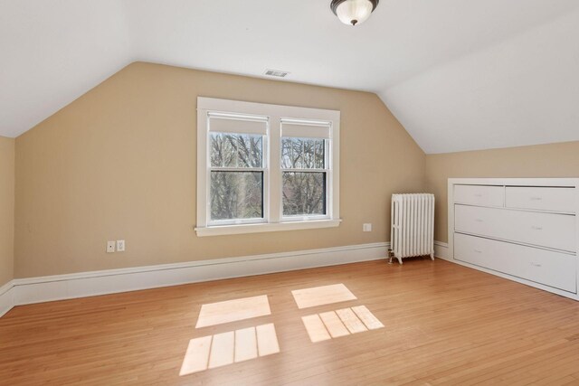 bonus room featuring visible vents, radiator, light wood-style floors, and lofted ceiling