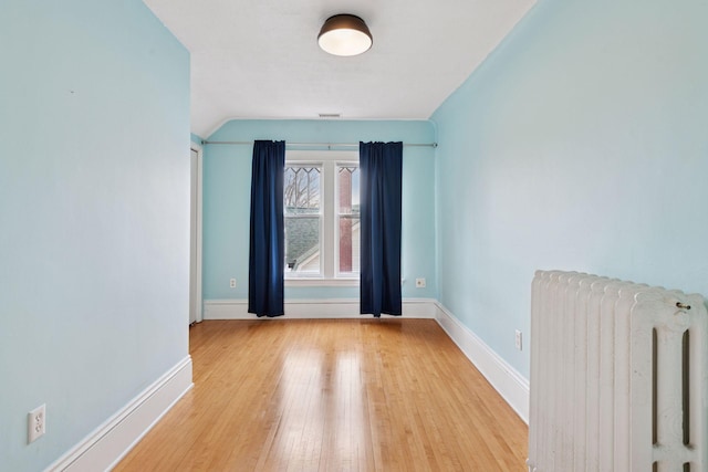spare room with visible vents, radiator heating unit, hardwood / wood-style flooring, and baseboards