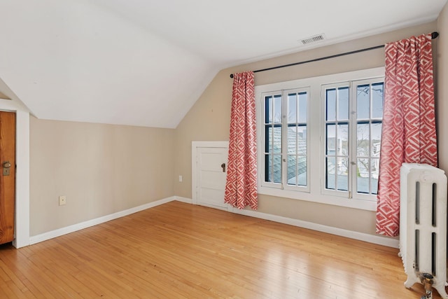 bonus room with visible vents, radiator heating unit, lofted ceiling, and light wood-type flooring
