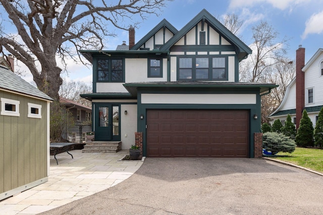 tudor home with a chimney, aphalt driveway, stucco siding, and an attached garage