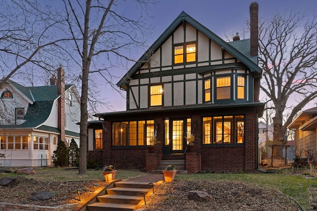 back of property at dusk with a chimney, brick siding, a porch, and stucco siding