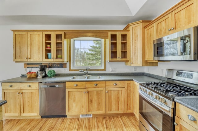 kitchen with visible vents, appliances with stainless steel finishes, dark countertops, a sink, and light wood-style floors