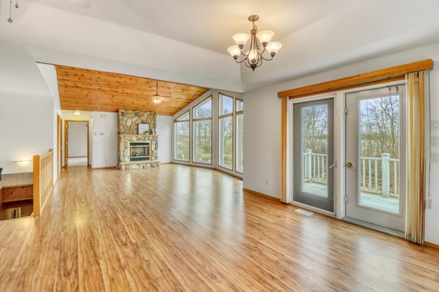 unfurnished living room with light wood-style floors, a chandelier, a stone fireplace, lofted ceiling, and visible vents