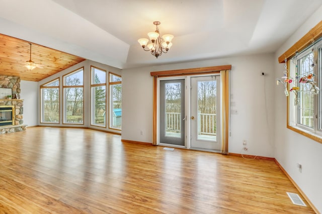 unfurnished living room featuring a chandelier, a stone fireplace, light wood-style flooring, lofted ceiling, and visible vents