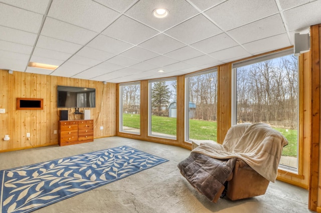 interior space with carpet flooring, a drop ceiling, and wooden walls