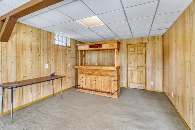 bar featuring baseboards, wood walls, and a paneled ceiling