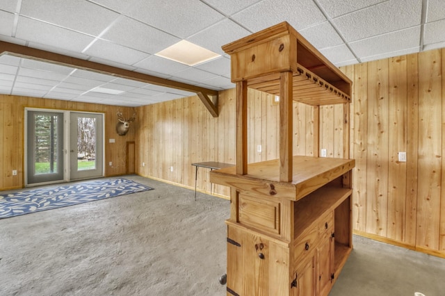 basement featuring carpet floors, baseboards, a drop ceiling, and wood walls