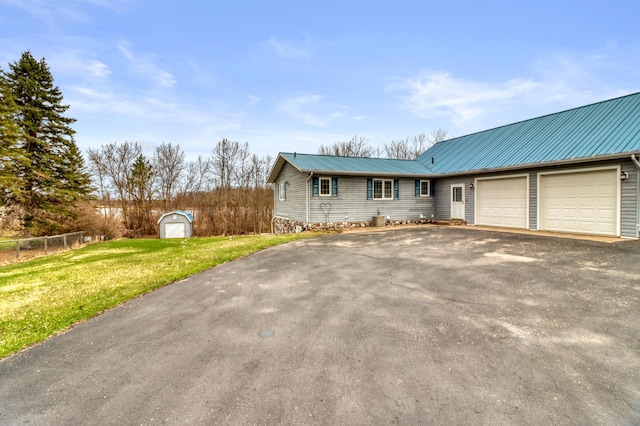 view of front facade featuring driveway, metal roof, a front yard, a garage, and a storage unit