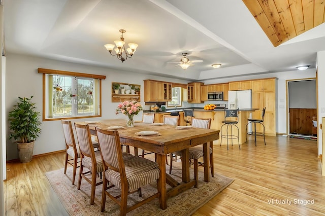 dining space featuring light wood-type flooring, a raised ceiling, ceiling fan with notable chandelier, and baseboards