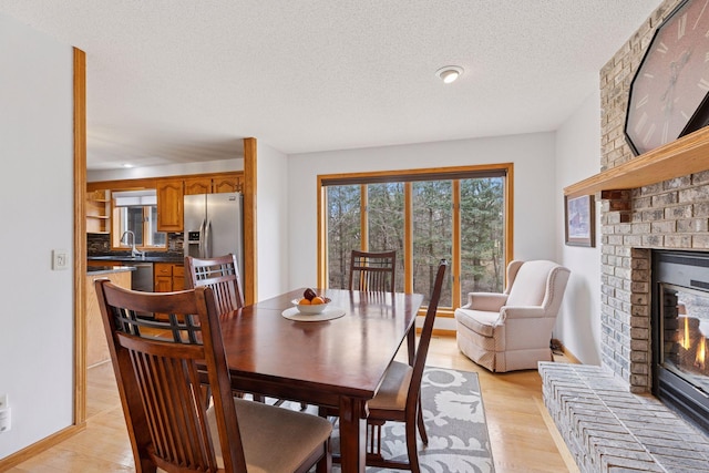 dining space with baseboards, light wood-type flooring, a brick fireplace, and a textured ceiling