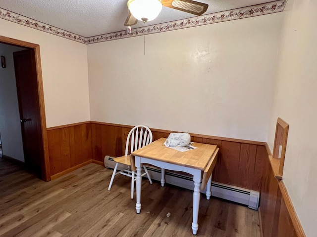 dining room with a ceiling fan, wood finished floors, a textured ceiling, wooden walls, and a wainscoted wall