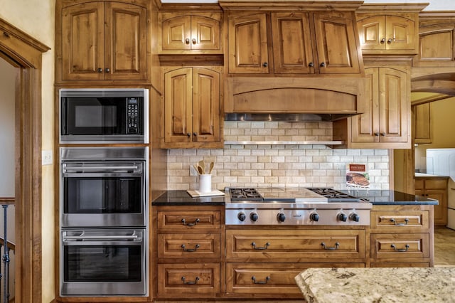kitchen featuring stainless steel appliances, dark stone countertops, brown cabinets, and decorative backsplash