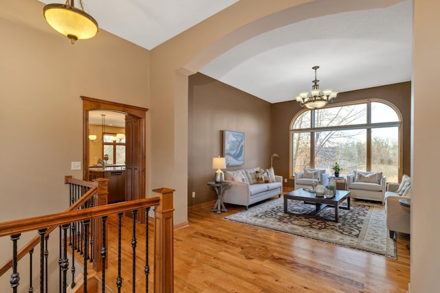 living area with a chandelier, arched walkways, light wood finished floors, vaulted ceiling, and baseboards