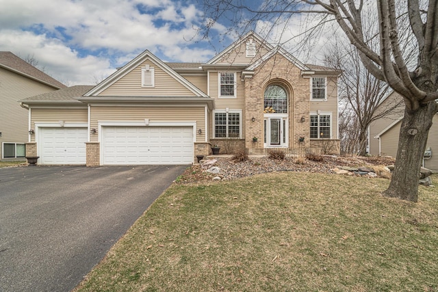 view of front facade featuring an attached garage, brick siding, aphalt driveway, and a front yard