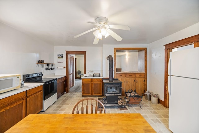 kitchen with white appliances, light countertops, brown cabinets, ceiling fan, and a wood stove