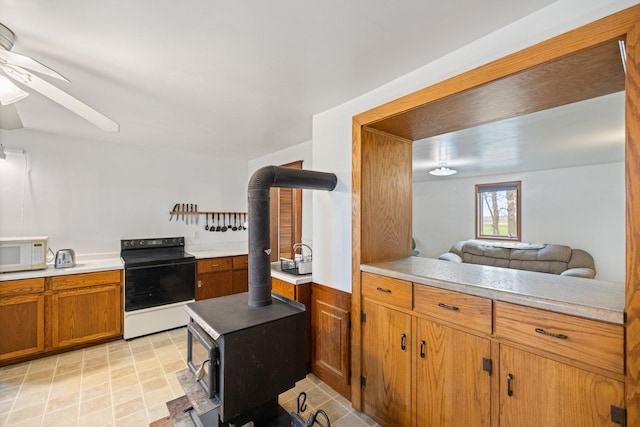 kitchen with white microwave, brown cabinets, ceiling fan, a wood stove, and black electric range oven