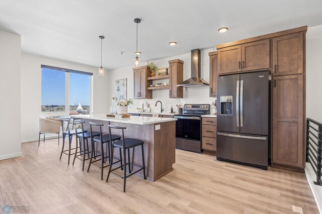 kitchen featuring a kitchen bar, appliances with stainless steel finishes, a center island, open shelves, and wall chimney exhaust hood