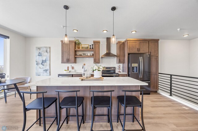 kitchen with open shelves, appliances with stainless steel finishes, wall chimney exhaust hood, and light wood-style floors