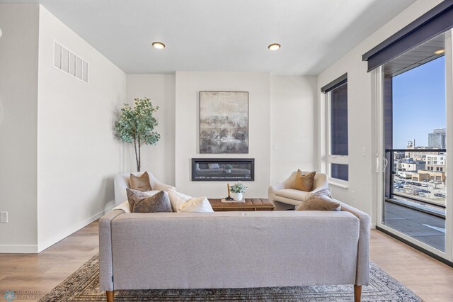 living room with a glass covered fireplace, recessed lighting, baseboards, wood finished floors, and visible vents