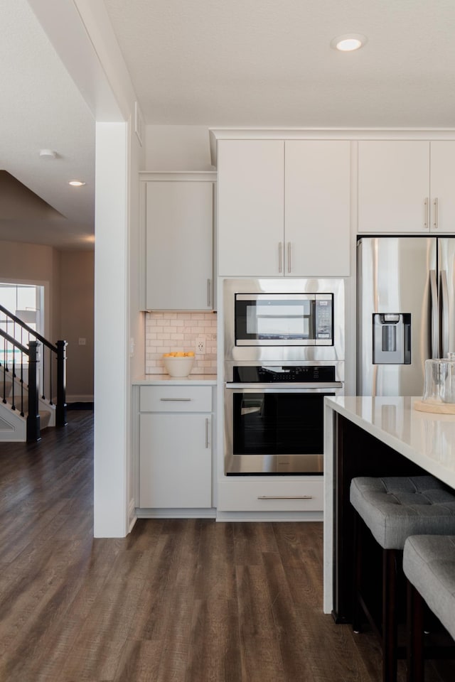 10155 Arrowwood Trl, Woodbury, MN 55129 - kitchen featuring stainless steel appliances, dark wood finished floors, light countertops, tasteful backsplash, and white cabinets