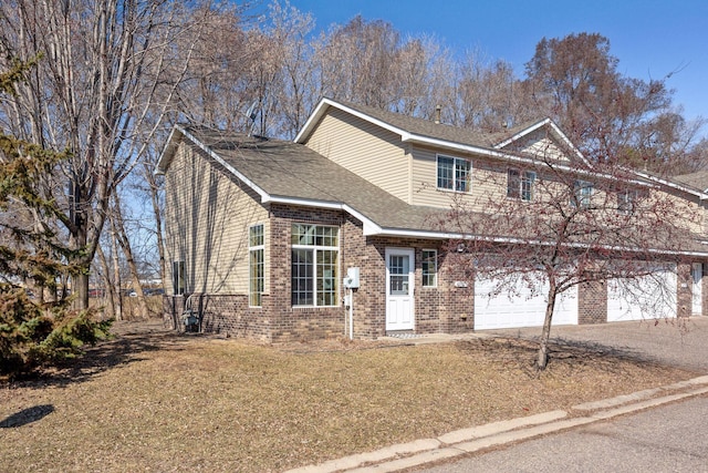 traditional-style house with roof with shingles, driveway, a front yard, and brick siding