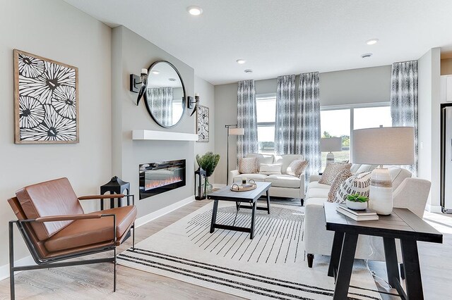 living room featuring baseboards, a glass covered fireplace, recessed lighting, and light wood-style floors